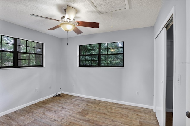 unfurnished bedroom featuring attic access, a textured ceiling, baseboards, and wood finished floors