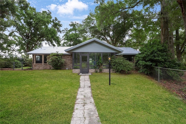 view of front of house with brick siding, a front yard, a sunroom, fence, and metal roof