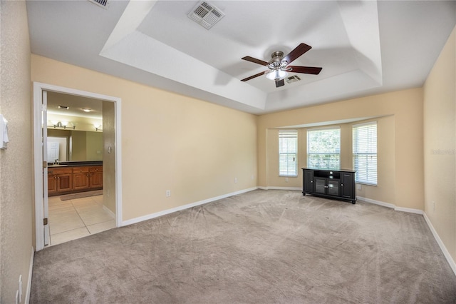 unfurnished living room with ceiling fan, light colored carpet, and a tray ceiling