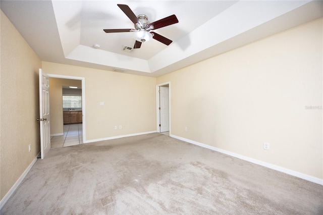 unfurnished bedroom featuring light carpet, ceiling fan, and a raised ceiling