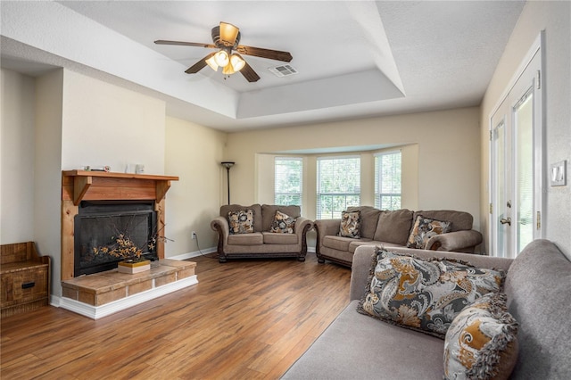 living room featuring wood-type flooring, a tray ceiling, ceiling fan, and a fireplace