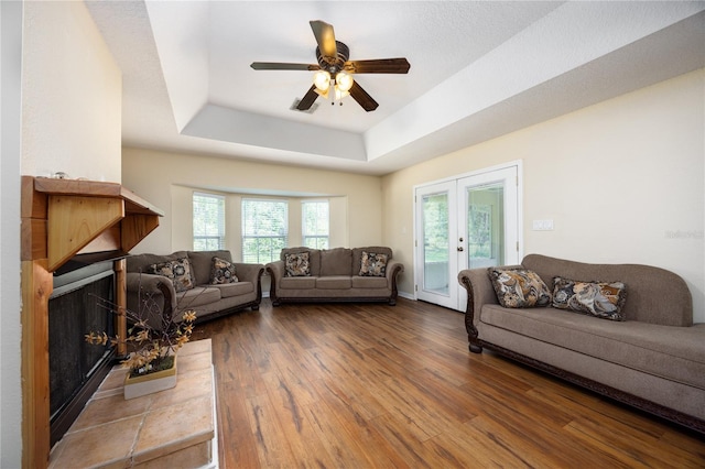 living room with ceiling fan, french doors, hardwood / wood-style flooring, a tray ceiling, and a tile fireplace