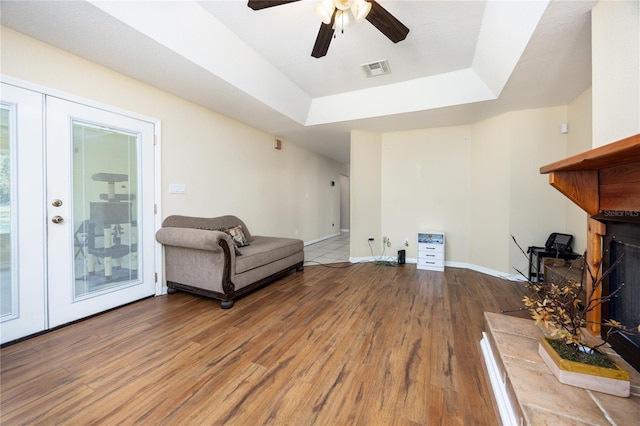 sitting room with wood-type flooring, ceiling fan, and a raised ceiling