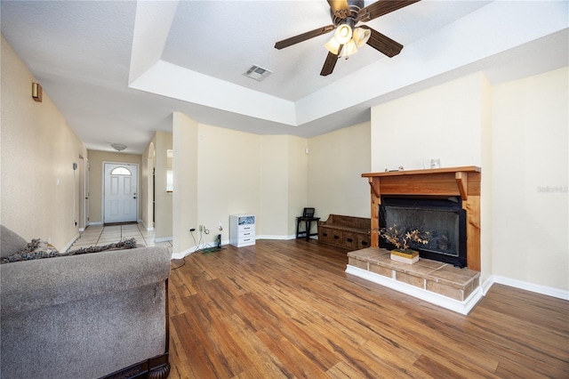 living room with a tiled fireplace, a textured ceiling, a tray ceiling, ceiling fan, and hardwood / wood-style flooring