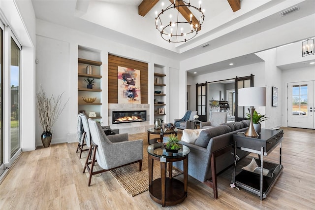 living room featuring a tiled fireplace, light hardwood / wood-style floors, beamed ceiling, built in shelves, and a chandelier