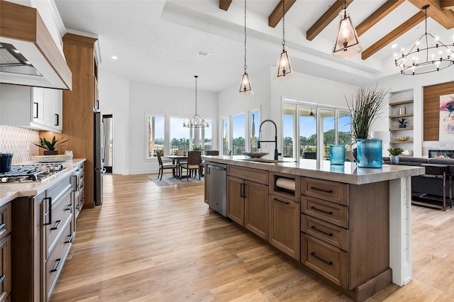 kitchen with a wealth of natural light, light wood-type flooring, custom range hood, an island with sink, and appliances with stainless steel finishes