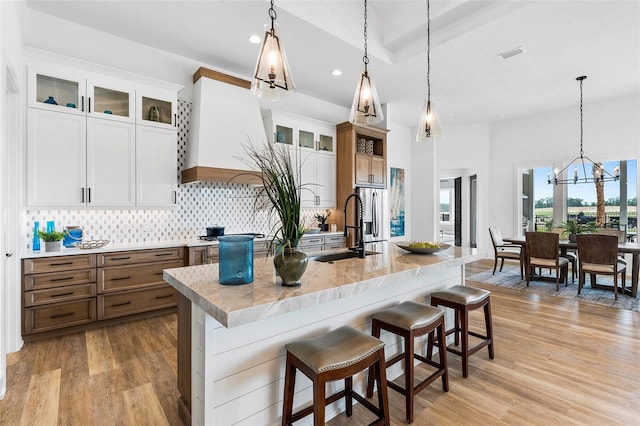 kitchen featuring tasteful backsplash, a center island with sink, decorative light fixtures, light wood-type flooring, and sink