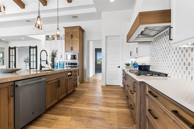 kitchen with tasteful backsplash, custom exhaust hood, decorative light fixtures, light wood-type flooring, and appliances with stainless steel finishes