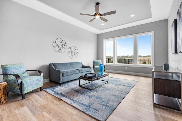 living room featuring a tray ceiling, ceiling fan, and light hardwood / wood-style flooring