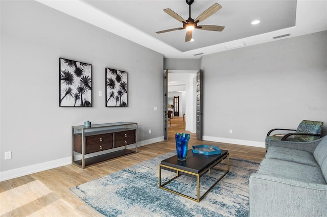 living room featuring a raised ceiling, ceiling fan, and hardwood / wood-style floors