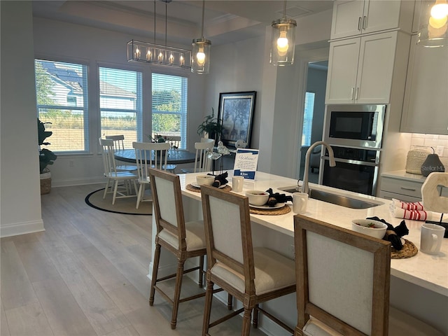 kitchen featuring white cabinetry, light hardwood / wood-style flooring, hanging light fixtures, and sink