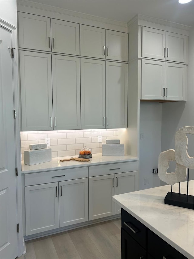 kitchen with decorative backsplash, light stone counters, white cabinetry, and light hardwood / wood-style flooring