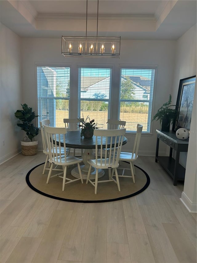 dining space with a notable chandelier, light wood-type flooring, crown molding, and a tray ceiling