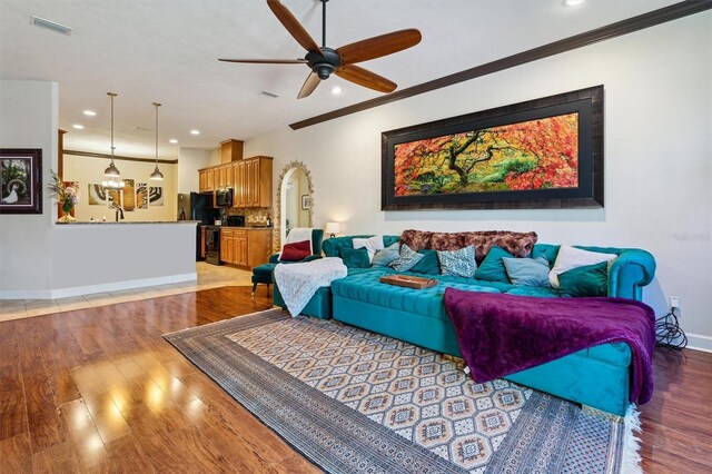 living room featuring hardwood / wood-style floors, ceiling fan, and crown molding