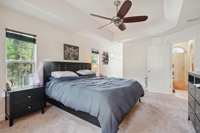 bedroom with light carpet, ceiling fan, a raised ceiling, and ensuite bathroom