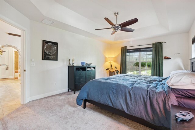 carpeted bedroom with a raised ceiling and ceiling fan