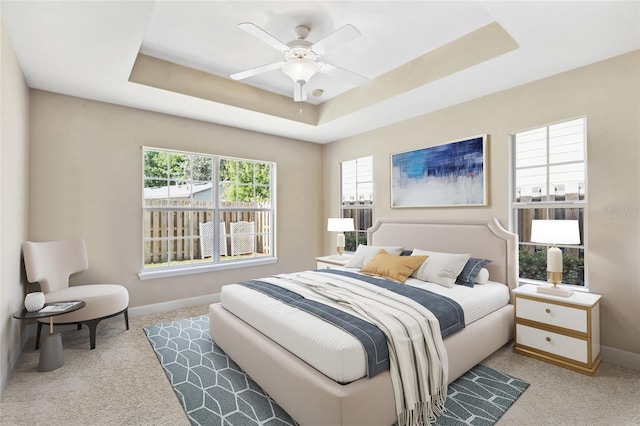 bedroom with ceiling fan, a tray ceiling, and light carpet