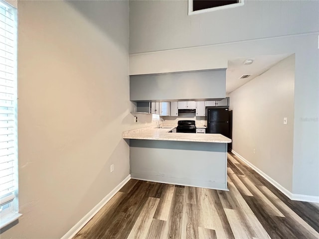 kitchen featuring sink, fume extractor, black appliances, kitchen peninsula, and hardwood / wood-style flooring