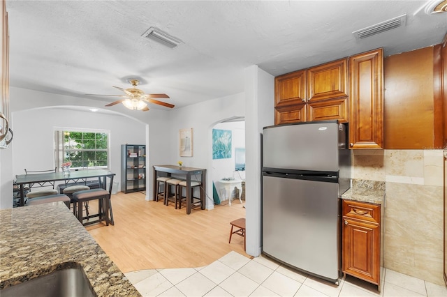 kitchen featuring stainless steel fridge, a textured ceiling, ceiling fan, light tile patterned floors, and dark stone countertops