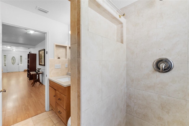 bathroom with tile patterned flooring, a tile shower, and vanity