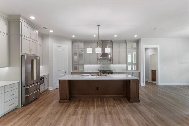 kitchen with high end refrigerator, decorative light fixtures, tasteful backsplash, and an island with sink