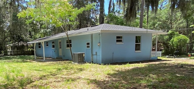 rear view of house with central AC and a lawn