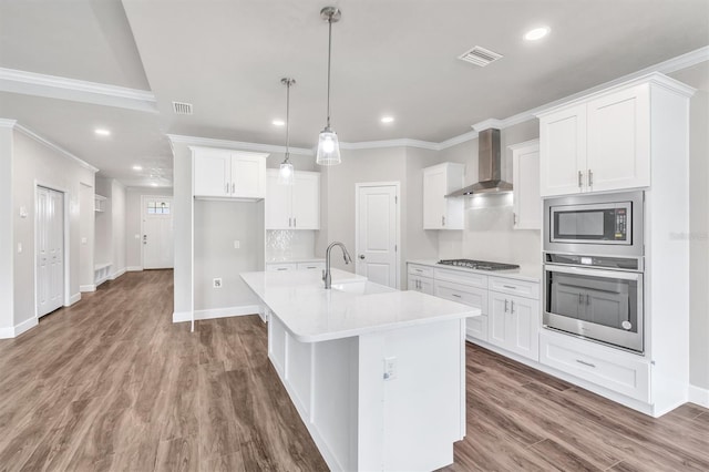 kitchen featuring wall chimney range hood, white cabinetry, appliances with stainless steel finishes, wood-type flooring, and sink