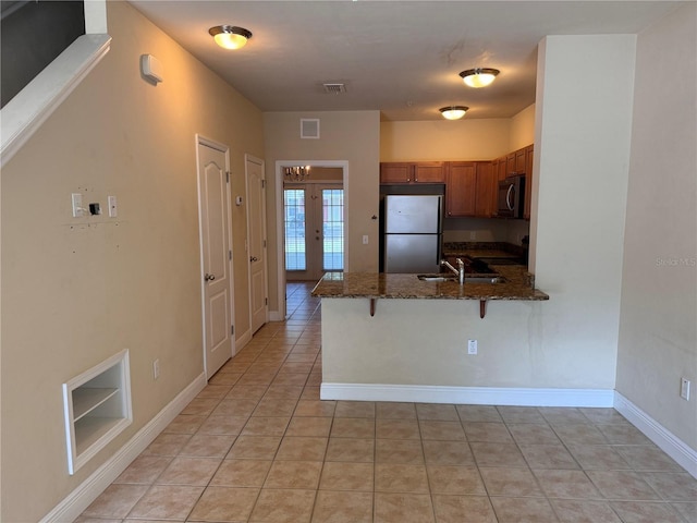 kitchen featuring light tile patterned flooring, dark stone counters, stainless steel appliances, kitchen peninsula, and a breakfast bar area