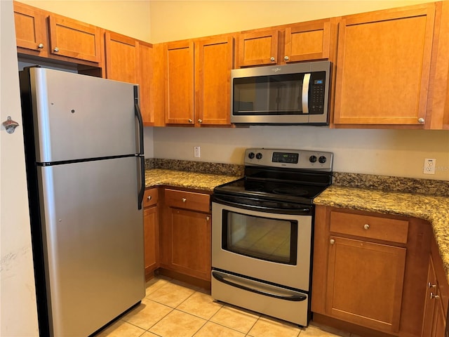 kitchen with light tile patterned flooring, appliances with stainless steel finishes, and dark stone counters