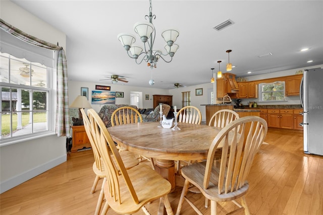 dining area featuring ceiling fan with notable chandelier, light wood-type flooring, a healthy amount of sunlight, and sink