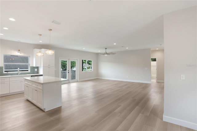 kitchen featuring tasteful backsplash, light wood-type flooring, pendant lighting, a kitchen island, and white cabinetry