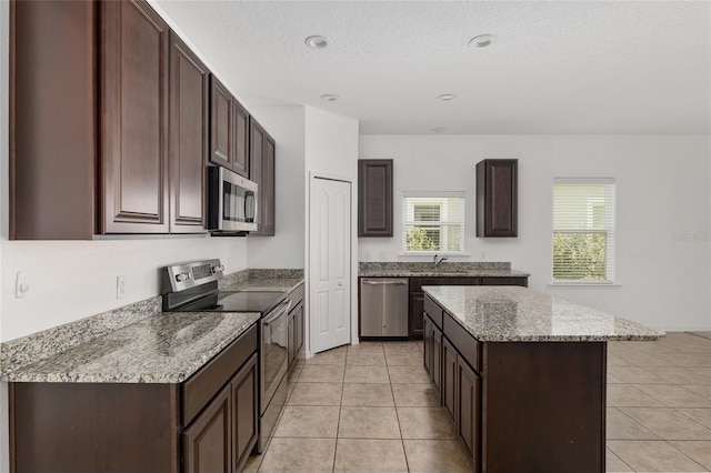 kitchen featuring stainless steel appliances, a center island, dark brown cabinets, sink, and light tile floors