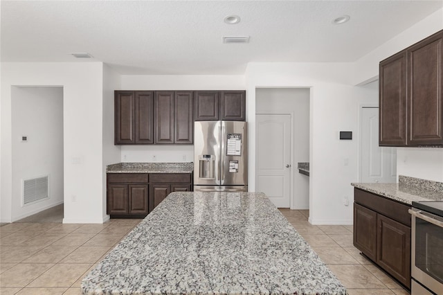 kitchen featuring appliances with stainless steel finishes, light stone countertops, light tile floors, and dark brown cabinetry