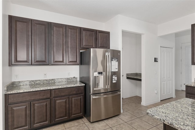 kitchen with dark brown cabinets, light stone counters, light tile flooring, and stainless steel fridge with ice dispenser