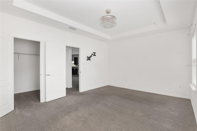 unfurnished bedroom with a raised ceiling, a closet, and dark carpet