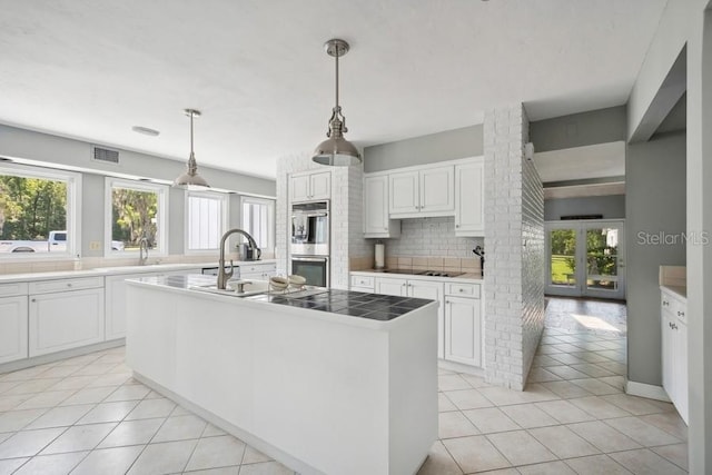 kitchen with pendant lighting, sink, an island with sink, tasteful backsplash, and white cabinetry