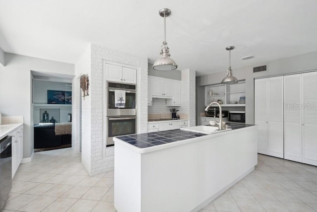 kitchen with a kitchen island with sink, white cabinetry, sink, and hanging light fixtures