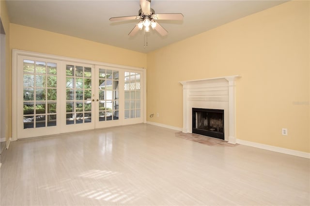 unfurnished living room featuring a tiled fireplace, ceiling fan, french doors, and light hardwood / wood-style flooring