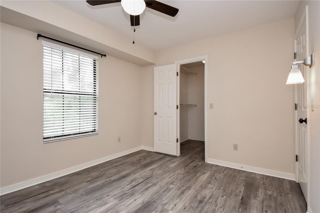 unfurnished bedroom with a walk in closet, ceiling fan, a closet, and multiple windows