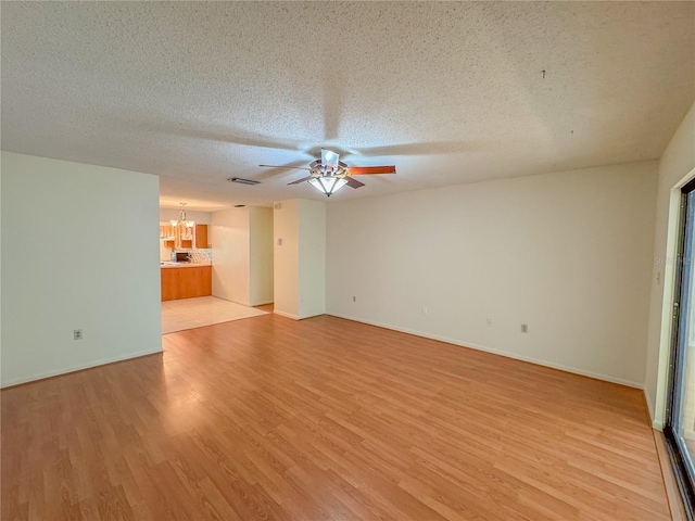 unfurnished living room featuring ceiling fan with notable chandelier, light hardwood / wood-style flooring, and a textured ceiling