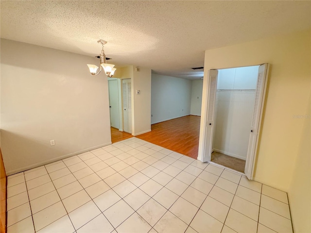 empty room featuring a chandelier, light hardwood / wood-style flooring, and a textured ceiling