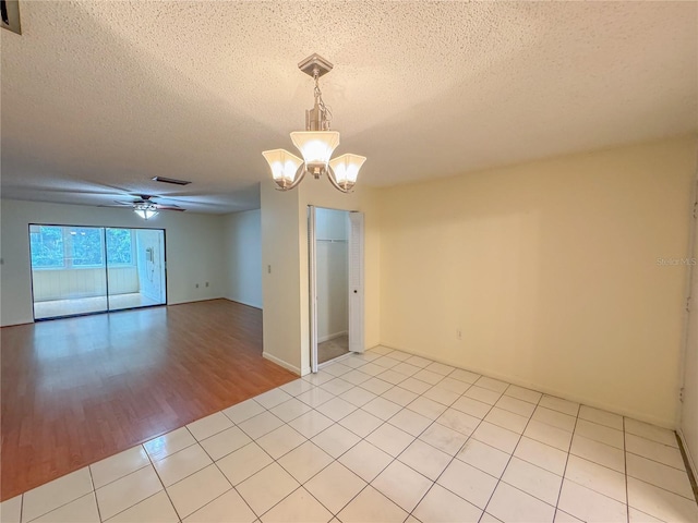 tiled spare room with a textured ceiling and ceiling fan with notable chandelier