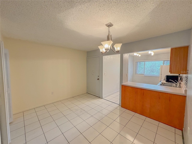 kitchen with a textured ceiling, an inviting chandelier, kitchen peninsula, decorative light fixtures, and light tile floors