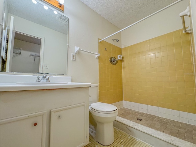 bathroom featuring tile flooring, a textured ceiling, a tile shower, toilet, and vanity