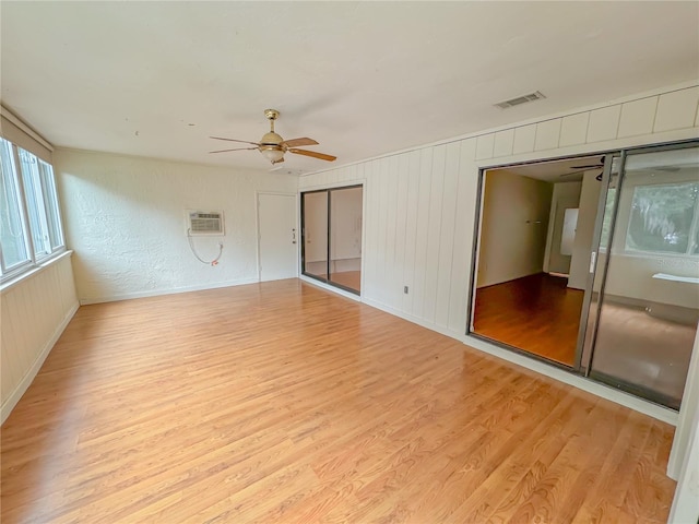 spare room with an AC wall unit, ceiling fan, and light wood-type flooring