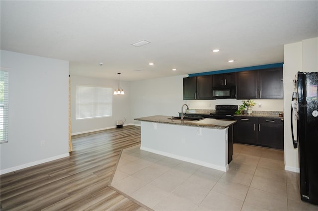 kitchen featuring a kitchen breakfast bar, an island with sink, black appliances, dark stone counters, and sink