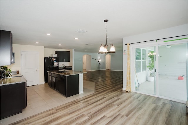 kitchen with light hardwood / wood-style floors, hanging light fixtures, a kitchen island with sink, light stone countertops, and sink