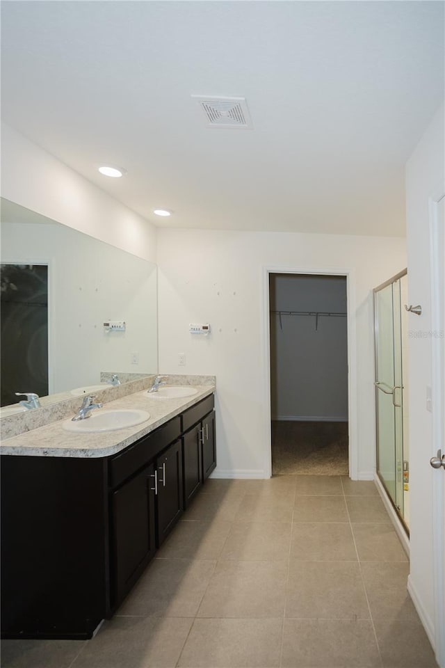 bathroom with a shower with shower door, large vanity, tile flooring, and double sink