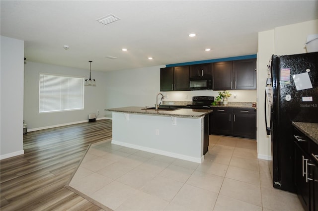 kitchen featuring light hardwood / wood-style flooring, an island with sink, black appliances, sink, and a breakfast bar area