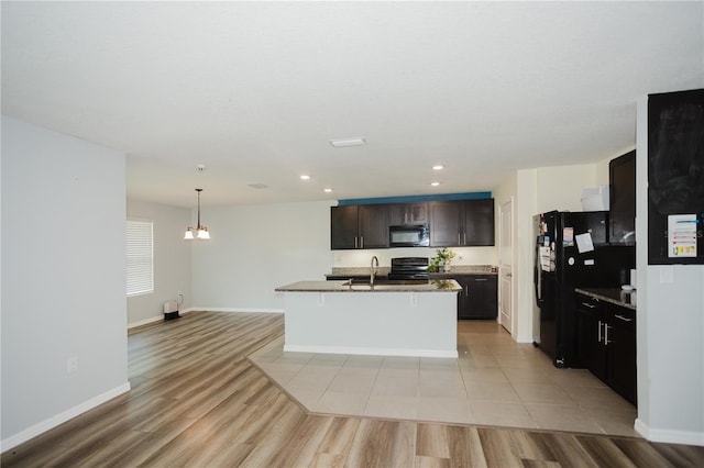 kitchen with black appliances, a kitchen island with sink, decorative light fixtures, dark brown cabinetry, and light tile floors